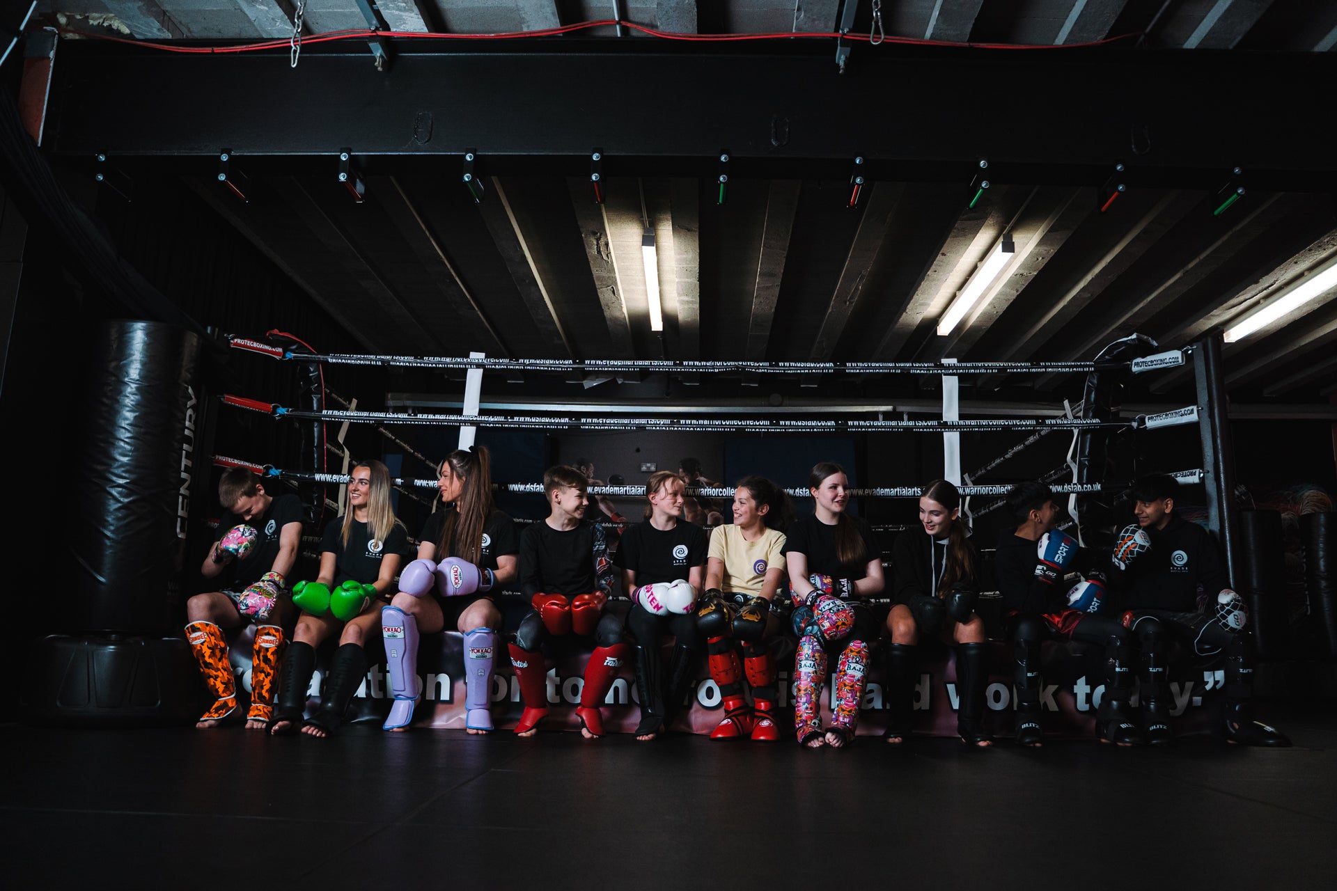 A photo of a number of Evade Martial Arts students sitting on the edge of the Kickboxing Tameside Boxing ring as part of the Evade Martial Arts Tameside and Children's Martial Arts Tameside programs